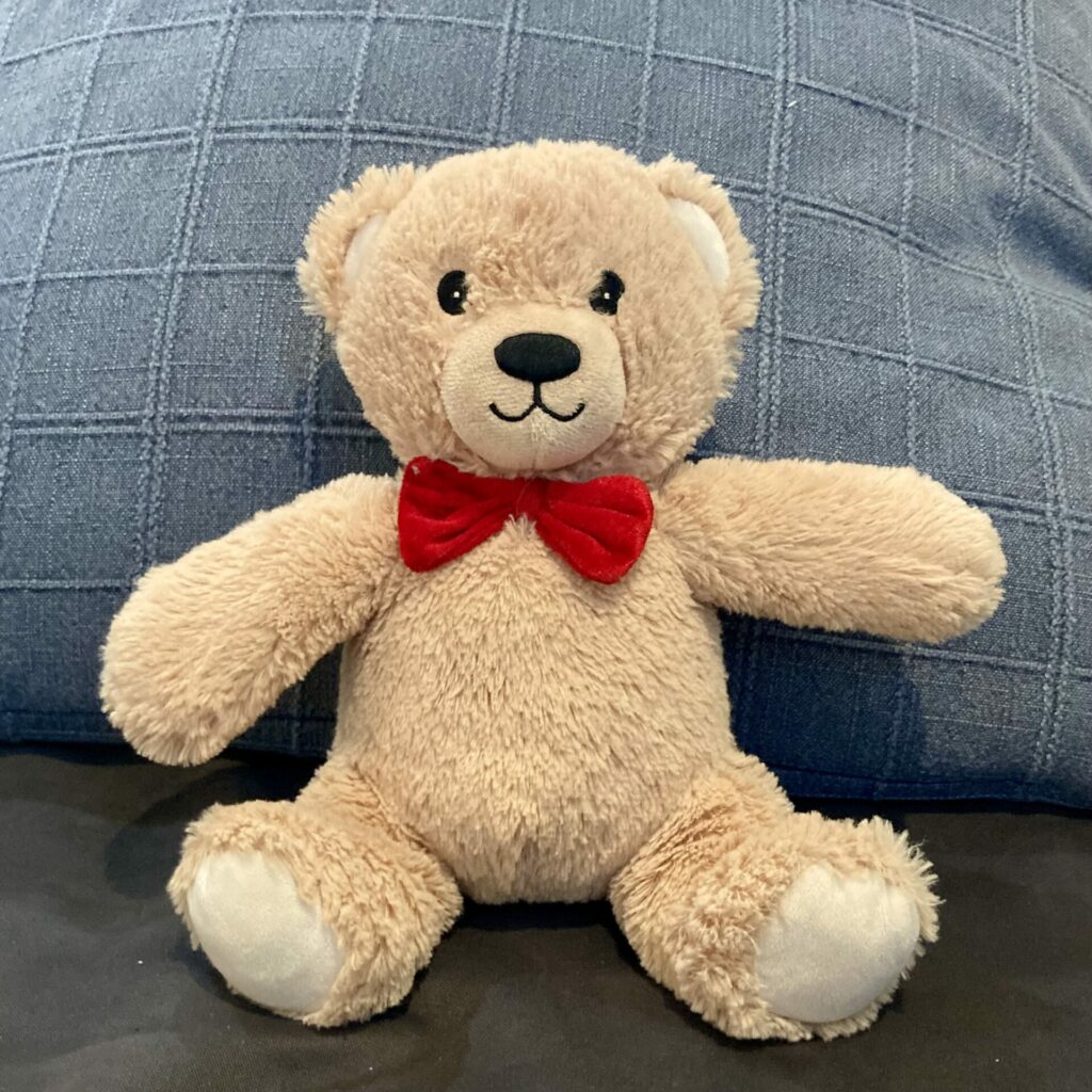 A classic light brown teddy bear with a red bow tie.