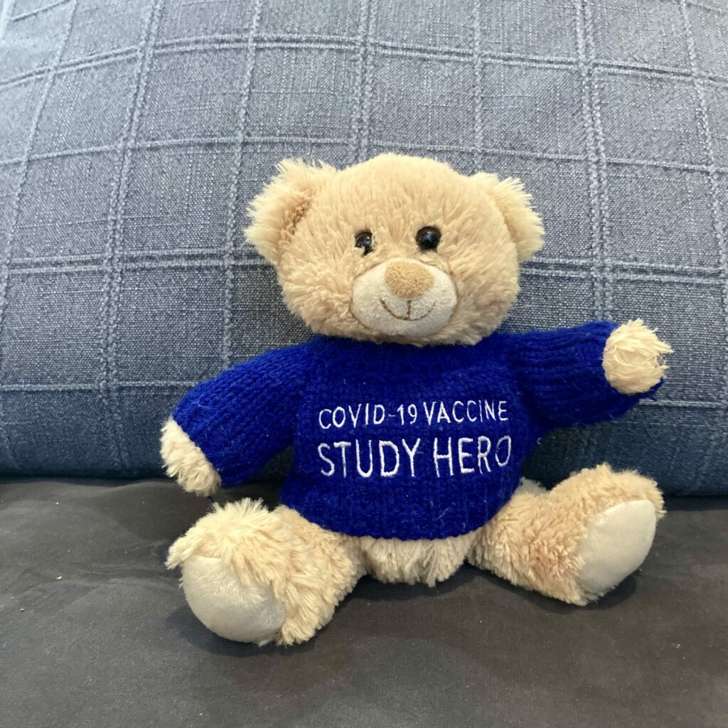 a teddy bear named bear bear wearing a blue sweater that says vaccine study hero