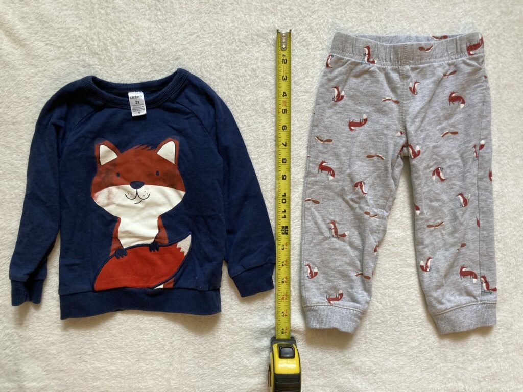 Toddler clothes with measuring tape beside them. There is a navy sweater with a fox on it and gray pants with little foxes all over it