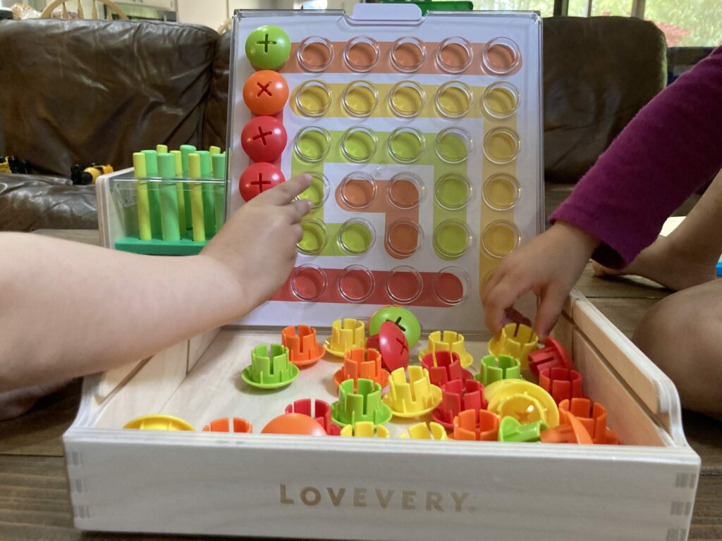 lovevery peg board toy that is wooden and has yellow, red, orange and green buttons you put in the board.