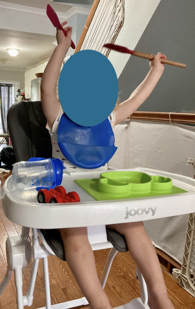 toddler with face blocked out in a joovy nook high chair
