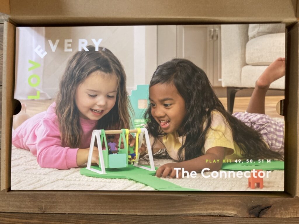 inside the lovevery connector play kit showing a picture of two girls playing with a toy swing set
