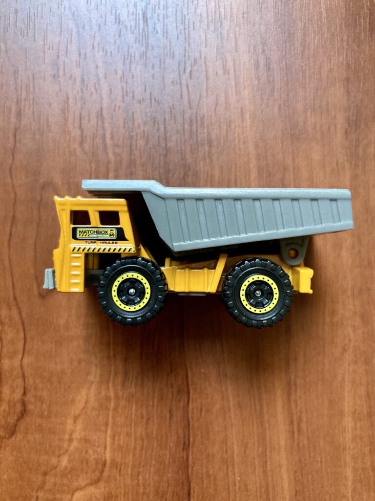 matchbox dump truck in side profile on a wood table. the truck is yellow and the dump is gray