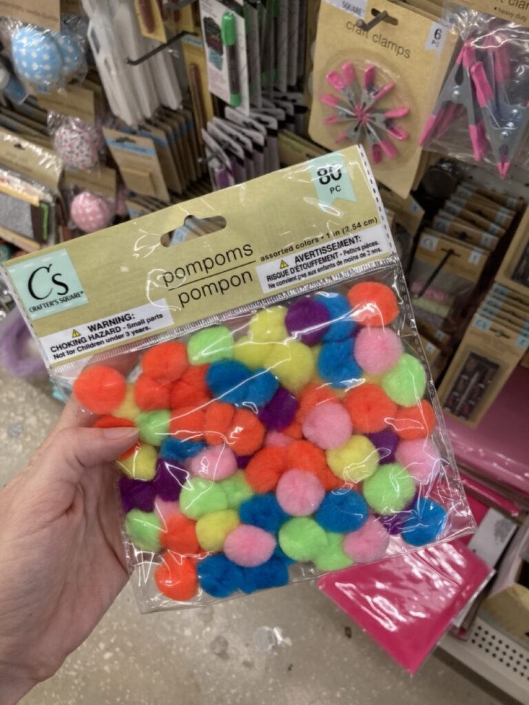 a hand holding a package of multicolor pom poms