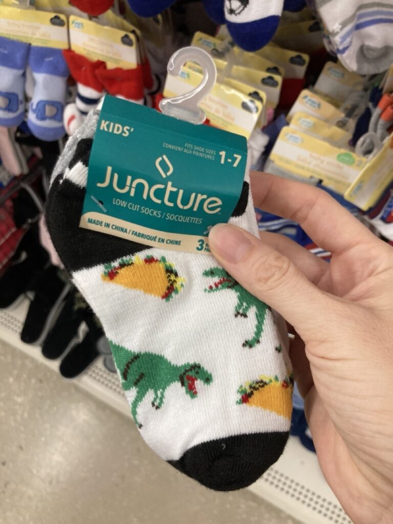 a pack of socks being held up by a hand. the socks have tacos and dinosaurs on them