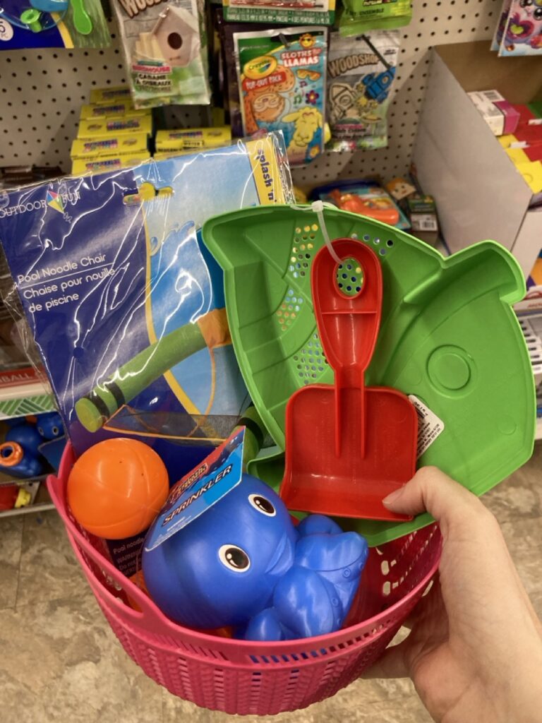 This picture is of a small plastic basket filled with beach toys being held by a hand in an aisle at the dollar tree