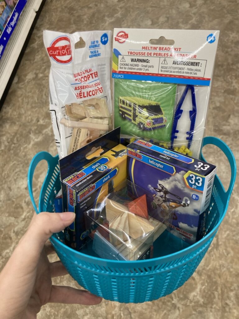 This picture is of a small plastic basket filled with STEM building kit toys being held by a hand in an aisle at the dollar tree