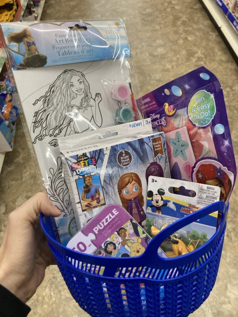 This picture is of a small plastic basket filled with disney-themed toys being held by a hand in an aisle at the dollar store