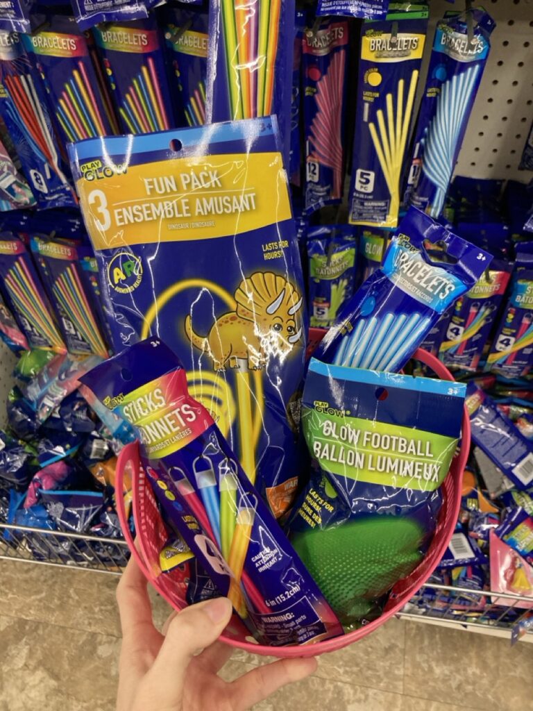 This picture is of a small plastic basket filled with glow sticks being held by a hand in an aisle at the dollar store