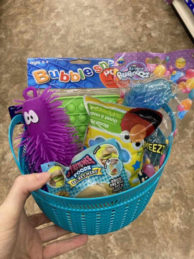This picture is of a small plastic basket filled with sensory toys being held by a hand in an aisle at the dollar tree