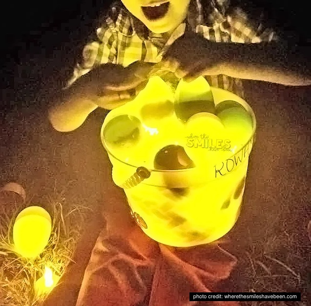 There is a bucket full of plastic Easter eggs that are glowing in the dark on a child's lap.