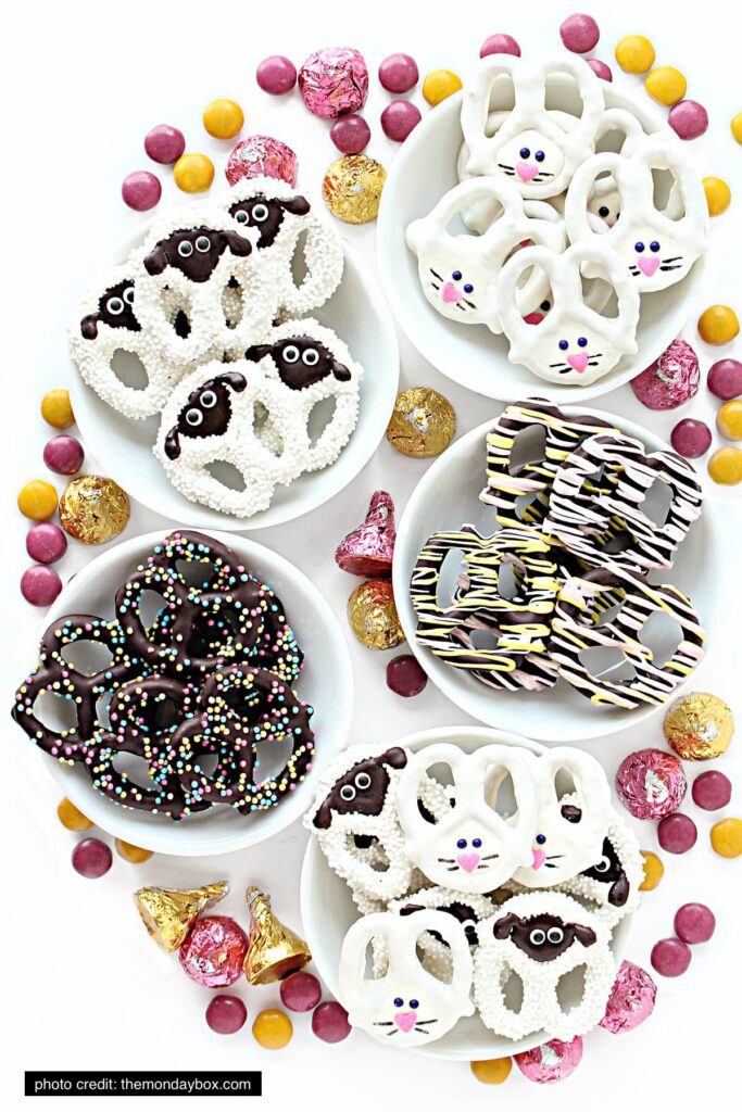 There are five bowls of decorated pretzels with candy around them. The pretzels are decorated like sheep and bunnies. 
