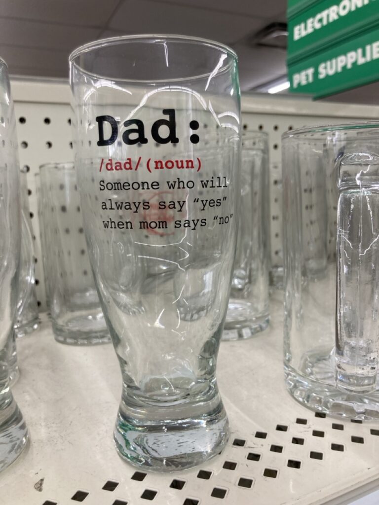 a glass pint glass on a shelf that says Dad on it