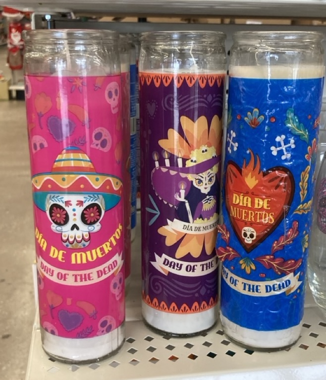 Three colorful Day of the Dead-themed prayer candles decorated with skulls and floral patterns in shades of pink, purple, and blue.
