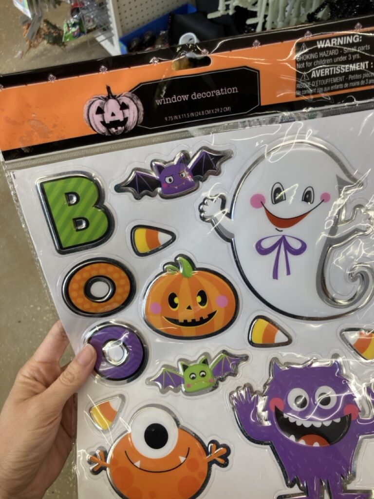 A pack of decorative pumpkin and bat stickers with glitter accents, held against a craft store backdrop.