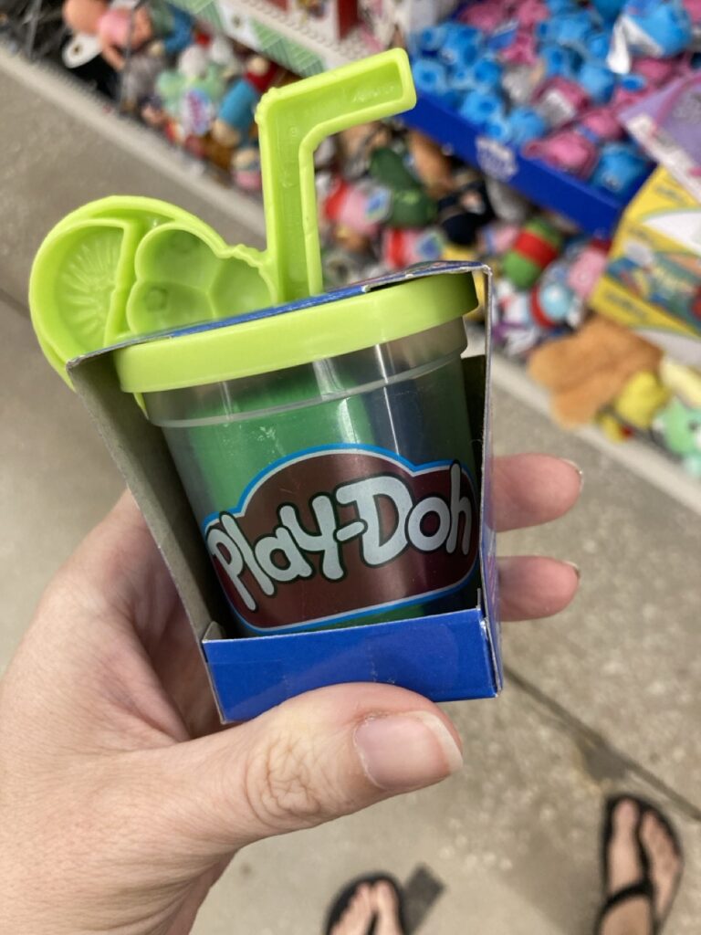 a hand holding a container of play doh with a store shelf in the background