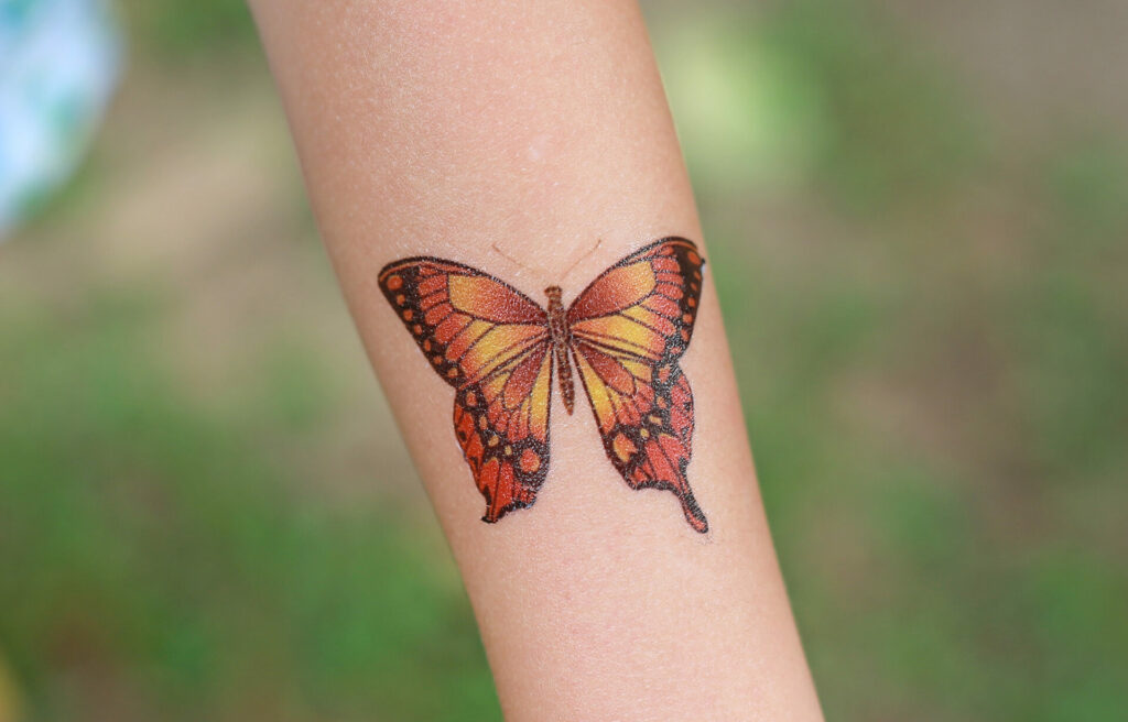 an arm with an orange butterfly tattoo on the inner arm