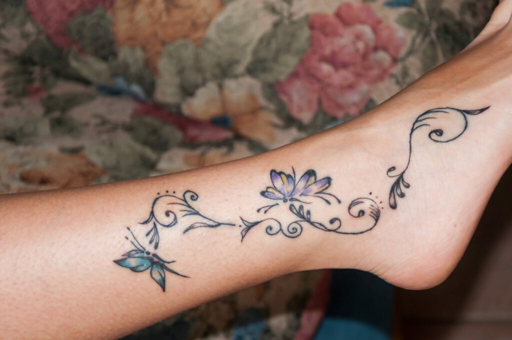 ankle tattoo with blue and pink butterflies with lines with leaves