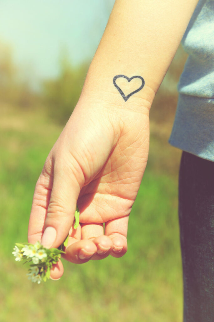 small heart tattoo on wrist with a hand holding a little yellow flower