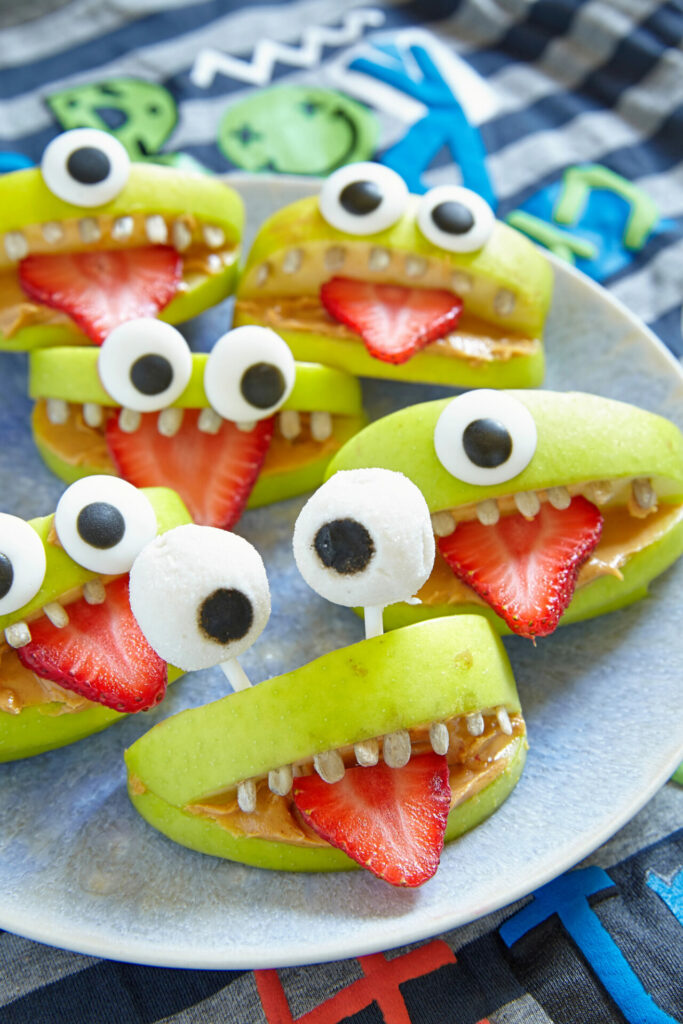 apple wedges cut to looks like monster faces with seeds for teeth and a strawberry tongue