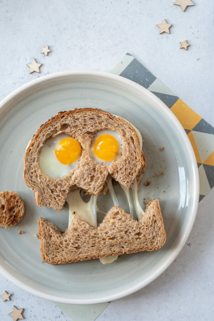 sandwich that looks like a monster with cheese pulling between the cut and eggs for eyes