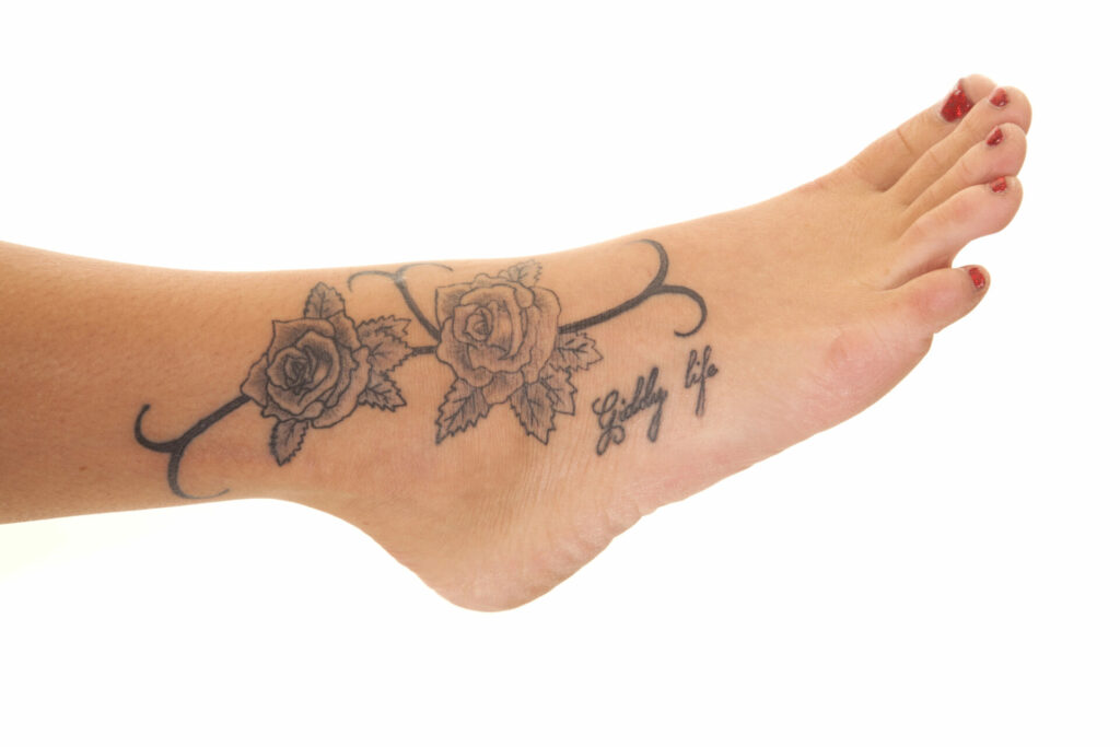 a foot tattoo of roses, hooks and the words giddy life