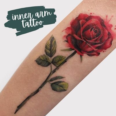a rose inner arm tattoo in red and green stem