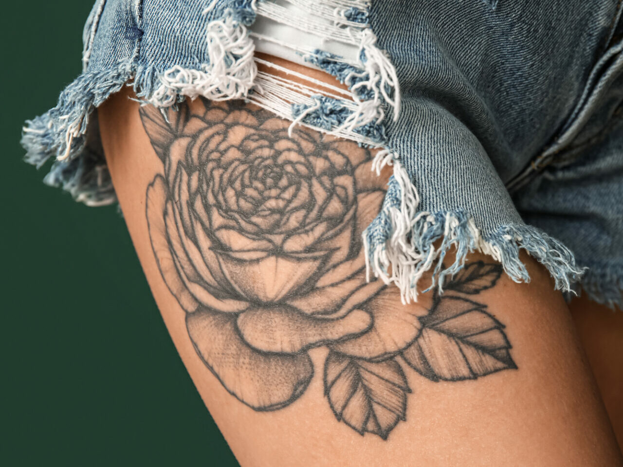 a big upper thigh rose tattoo peaking out from cut off jeans