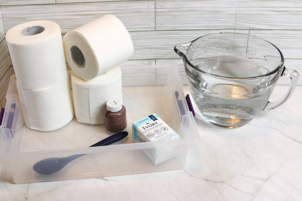 Roll of toilet aers, measuring cup with water, paint bottle, spatula, and empty clear container.