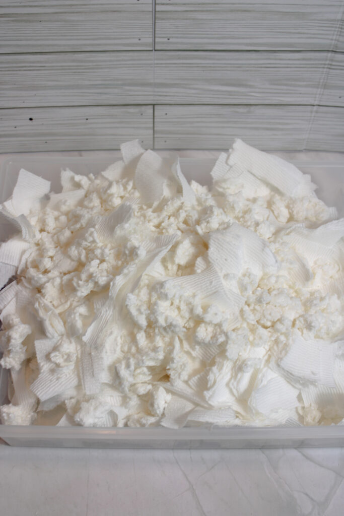 Mixed melted bar of soap and shredded toilet paper inside a clear plastic container.
